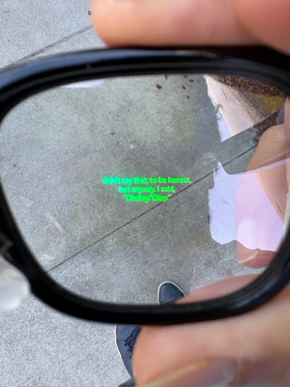 A close-up view through caption glasses showing bright green real-time text