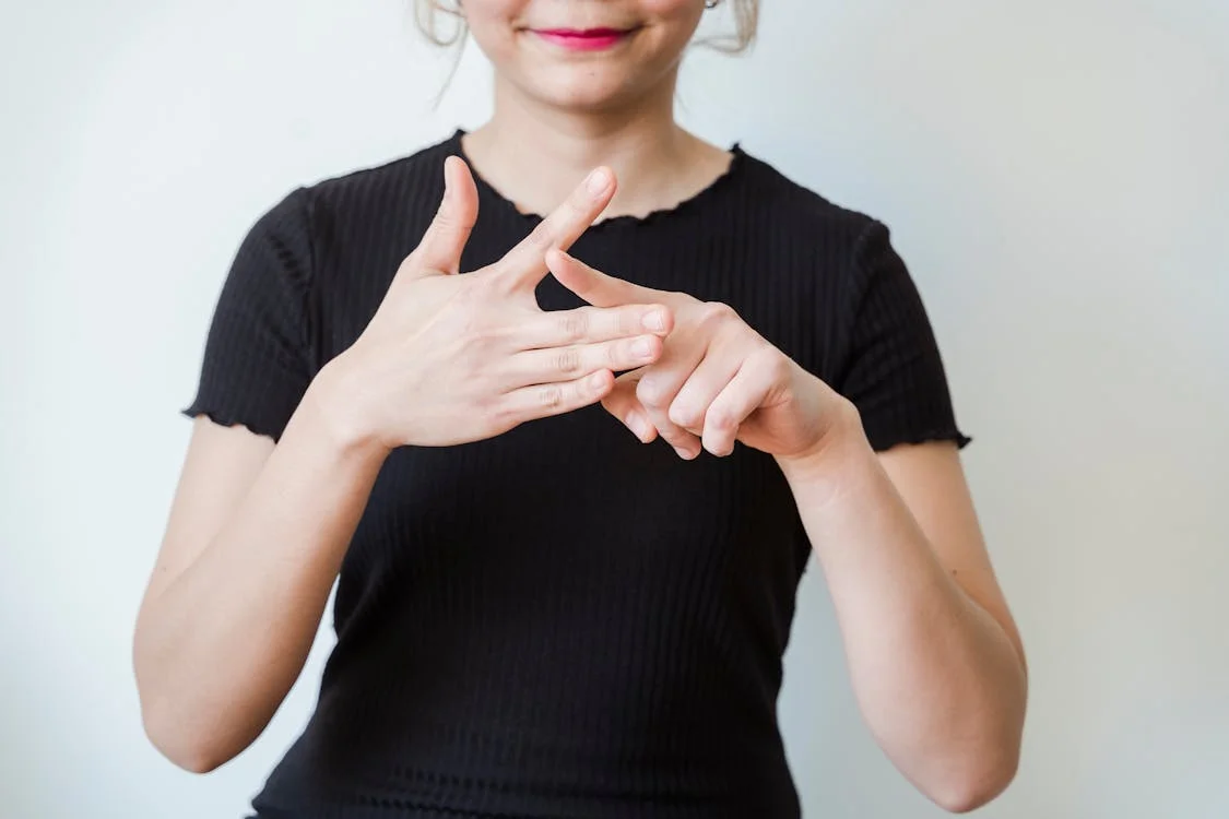 Woman demonstrating sign language hand gestures, representing the deaf and hard-of-hearing community that captioning glasses serve