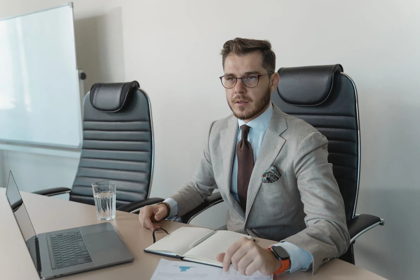 A businessman in eyeglasses and a suit concentrating during an office meeting, illustrating the high-stakes professional scenarios where captioning glasses help cochlear implant users follow rapid turn-taking