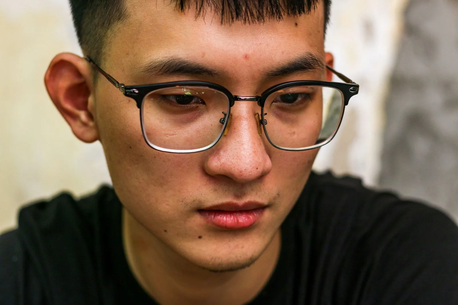 Close-up portrait of a thoughtful young adult in eyeglasses turning their head slightly to listen, representing single-sided deafness and the daily habit of leading with the hearing ear