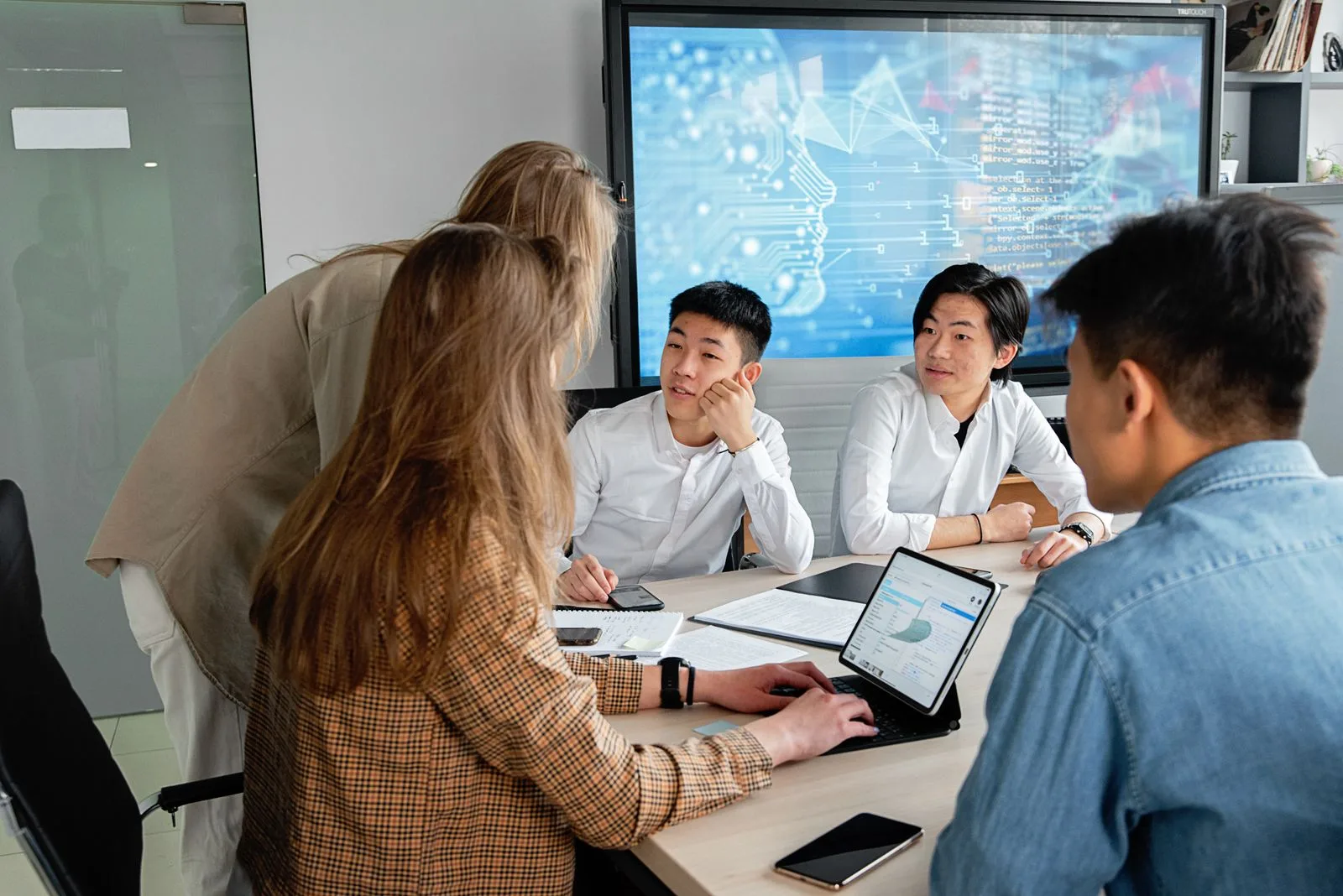 A team of professionals collaborating around a table in a modern office meeting, illustrating the multi-speaker, rapid turn-taking scenarios where captioning glasses help single-sided deafness listeners keep pace