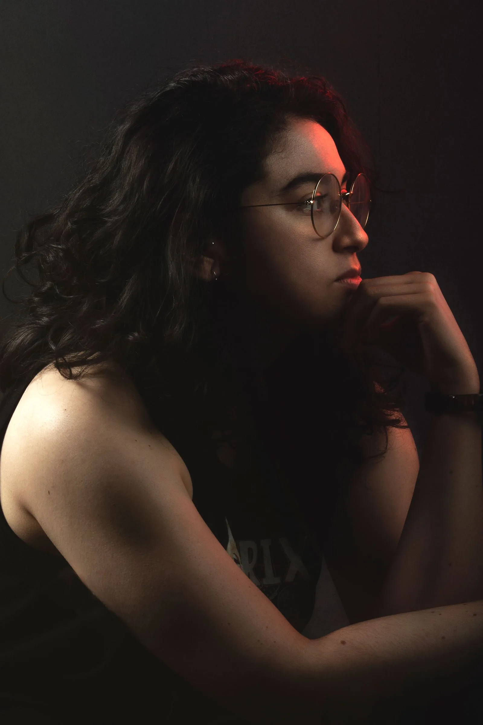 A woman in eyeglasses photographed in dramatic side lighting, gazing off-camera in a moment of focused listening, illustrating the concentrated attention single-sided deafness demands