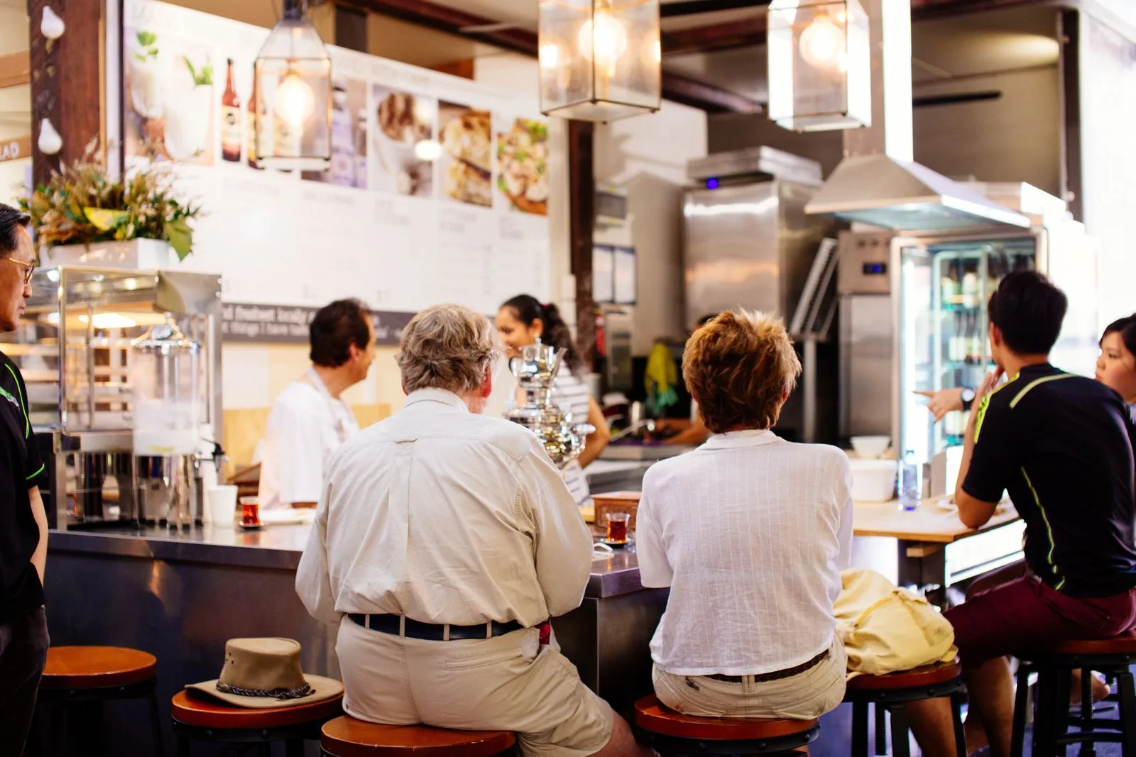 A busy contemporary restaurant with diners seated at tables and pendant lighting overhead, representing the noisy multi-talker environments where single-sided deafness listeners struggle most